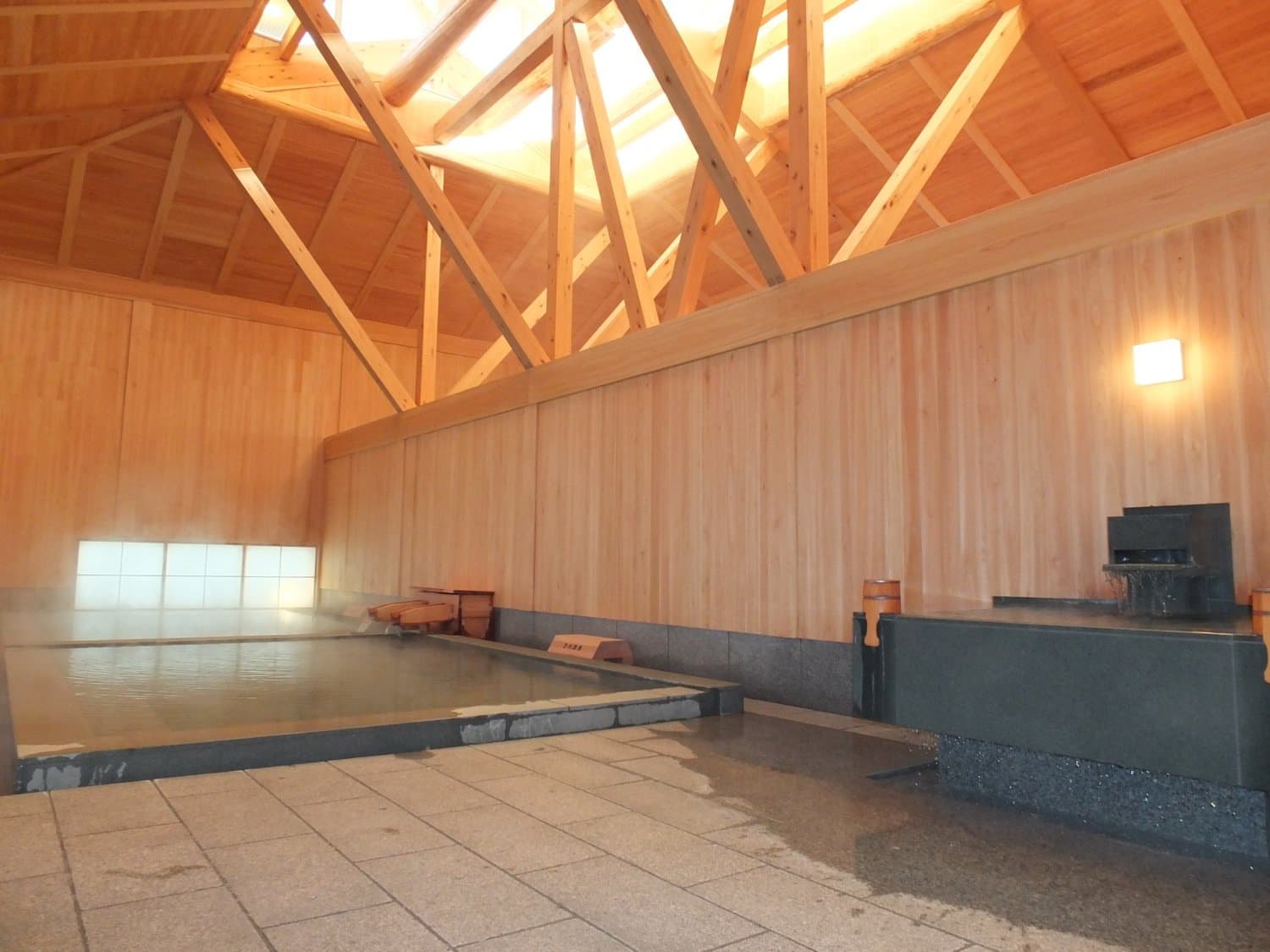 An indoor hot-spring bath with a timber-beamed ceiling and milky water in Kusatsu